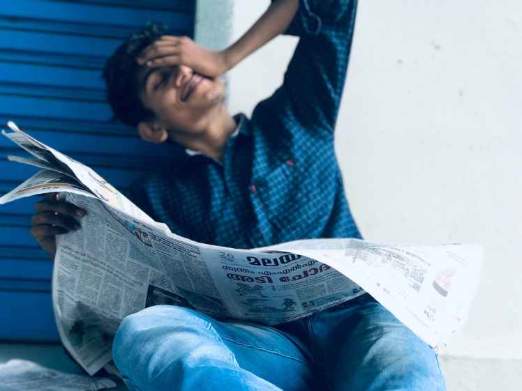 photo of a man sitting while holding newspaper